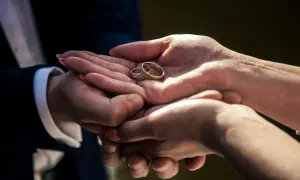 Dłonie pary trzymające dwie złote obrączki ślubne.