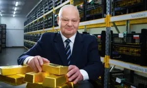 Mężczyzna w garniturze w magazynie Narodowego Banku Polskiego, otoczony sztabkami złota, sugeruje, ile złota ma Polska.