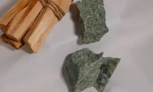 Surowe bryłki zielonego jadeitu, kamienia o licznych właściwościach, leżą obok wiązki drewna palo santo.