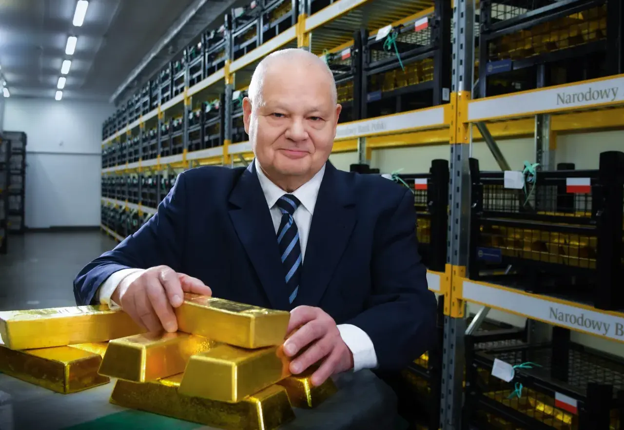 Mężczyzna w garniturze w magazynie Narodowego Banku Polskiego, otoczony sztabkami złota, sugeruje, ile złota ma Polska.