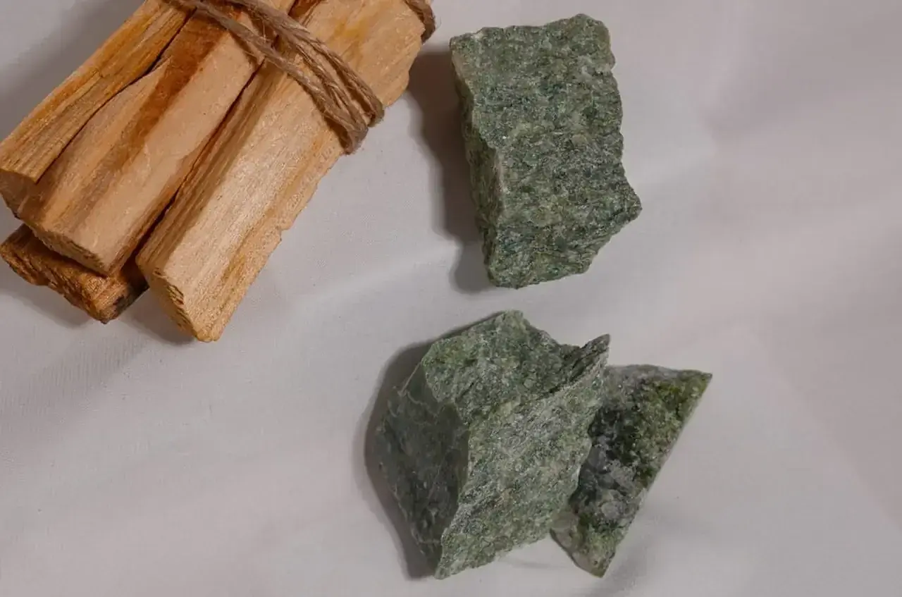 Surowe bryłki zielonego jadeitu, kamienia o licznych właściwościach, leżą obok wiązki drewna palo santo.