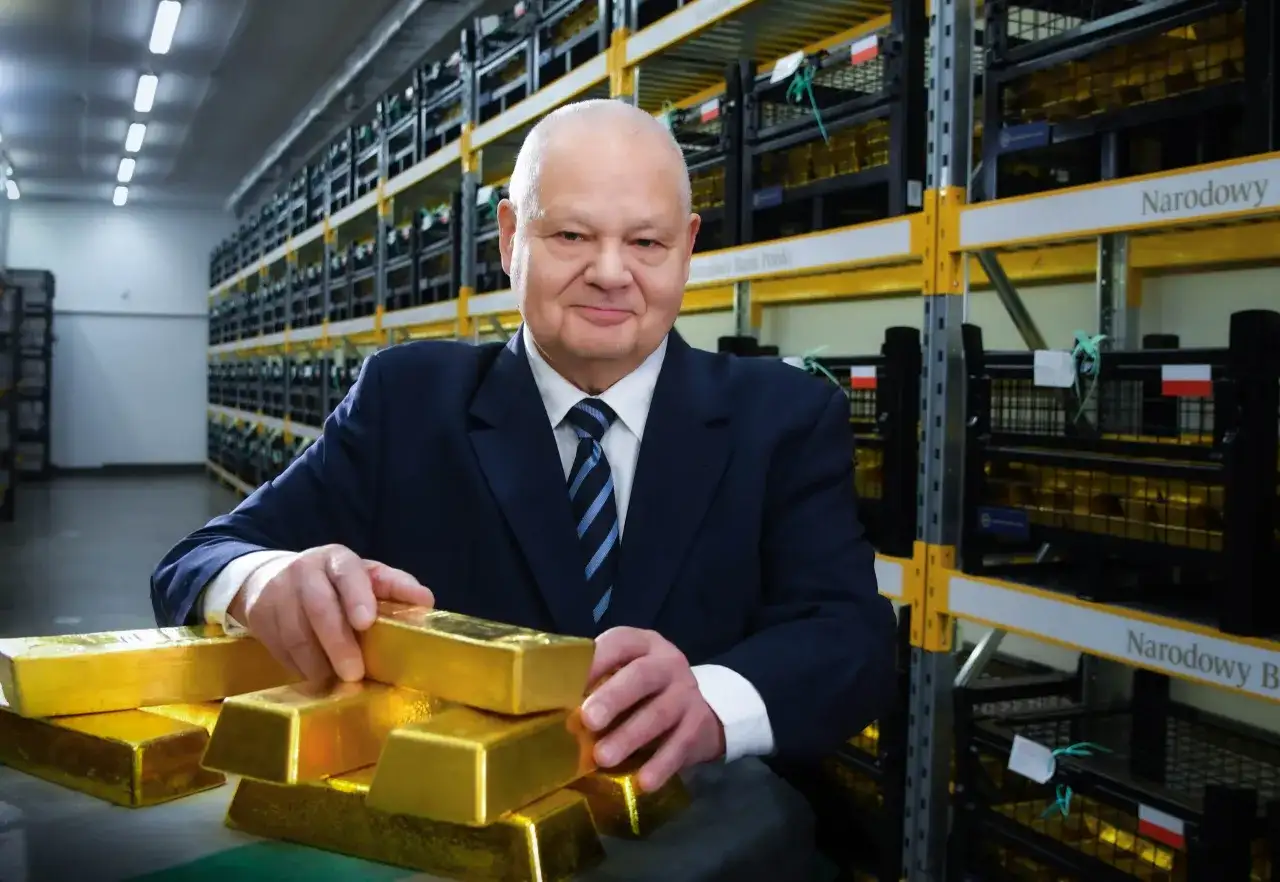 Mężczyzna w garniturze w magazynie Narodowego Banku Polskiego, otoczony sztabkami złota, sugeruje, ile złota ma Polska.